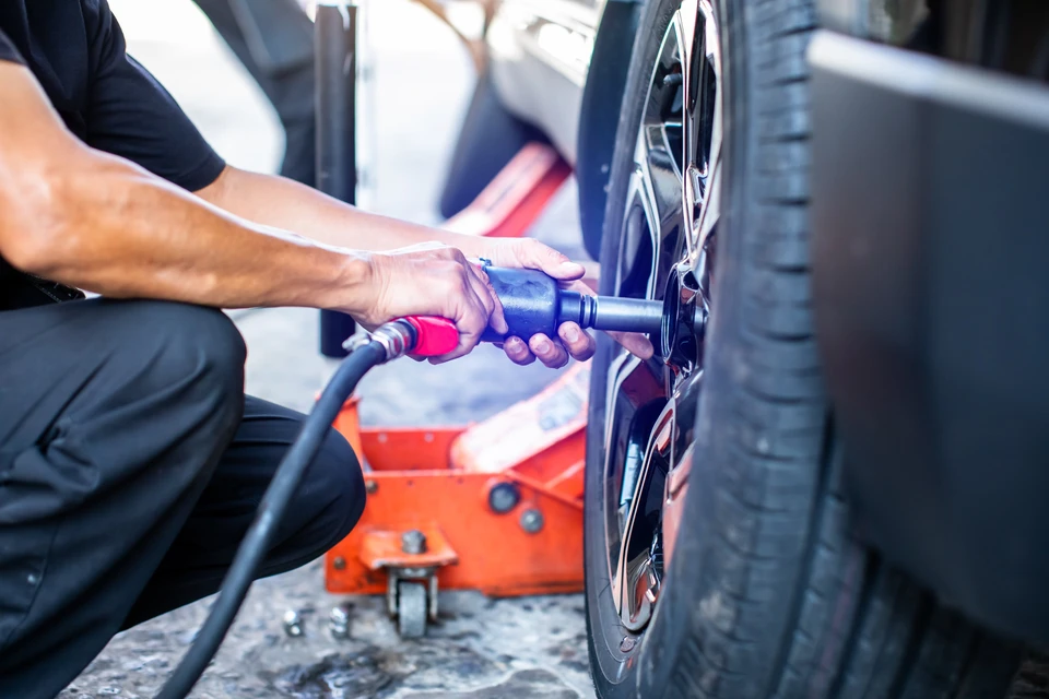 Homme utilisant un outil pneumatique pour démonter une roue de voiture dans un garage automobile