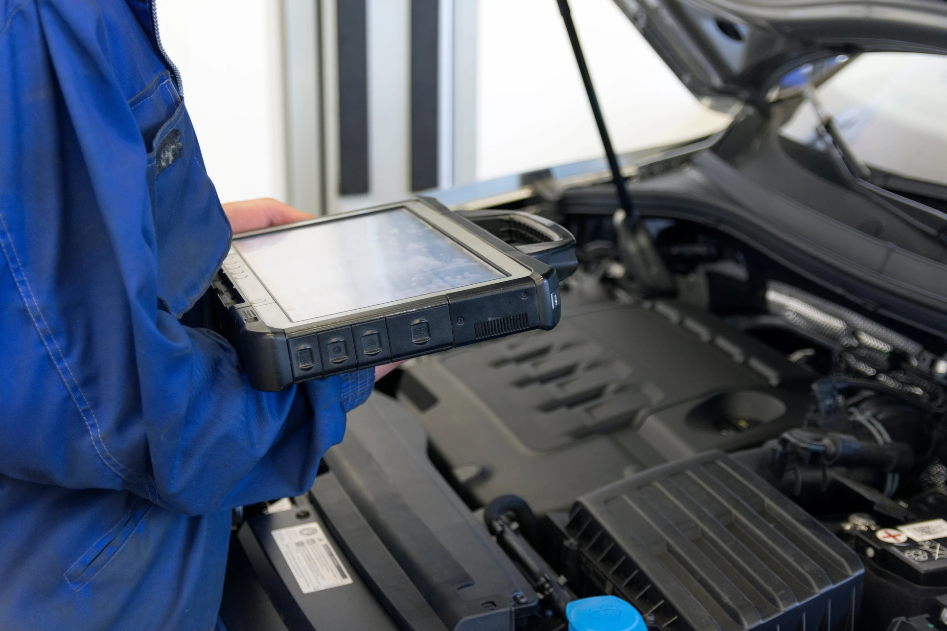 Un mécanicien automobile en combinaison bleue utilise une tablette de diagnostic dans un garage