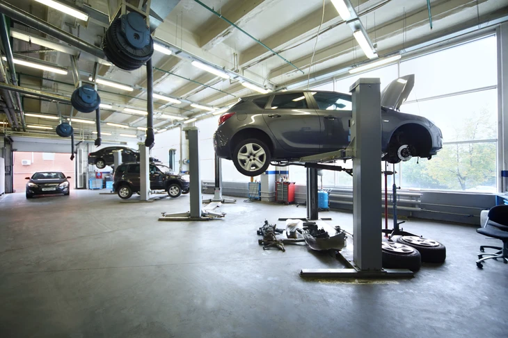 Mécanicien automobile travaillant sous le capot ouvert d'une voiture blanche dans un garage professionnel