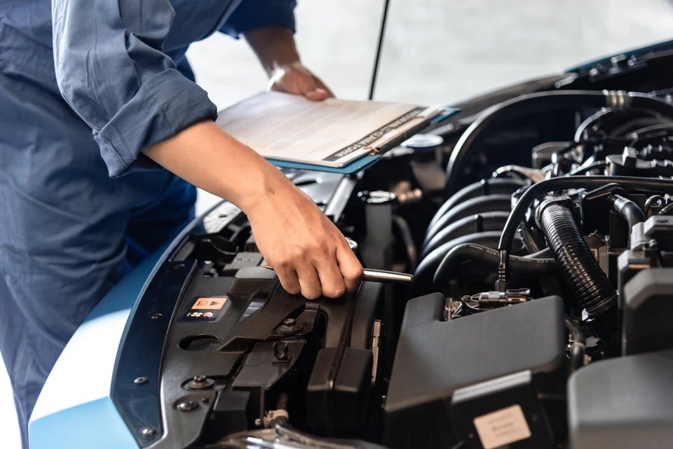 Mécanicien automobile travaillant sous le capot d'un véhicule, effectuant une intervention technique avec un outil manuel