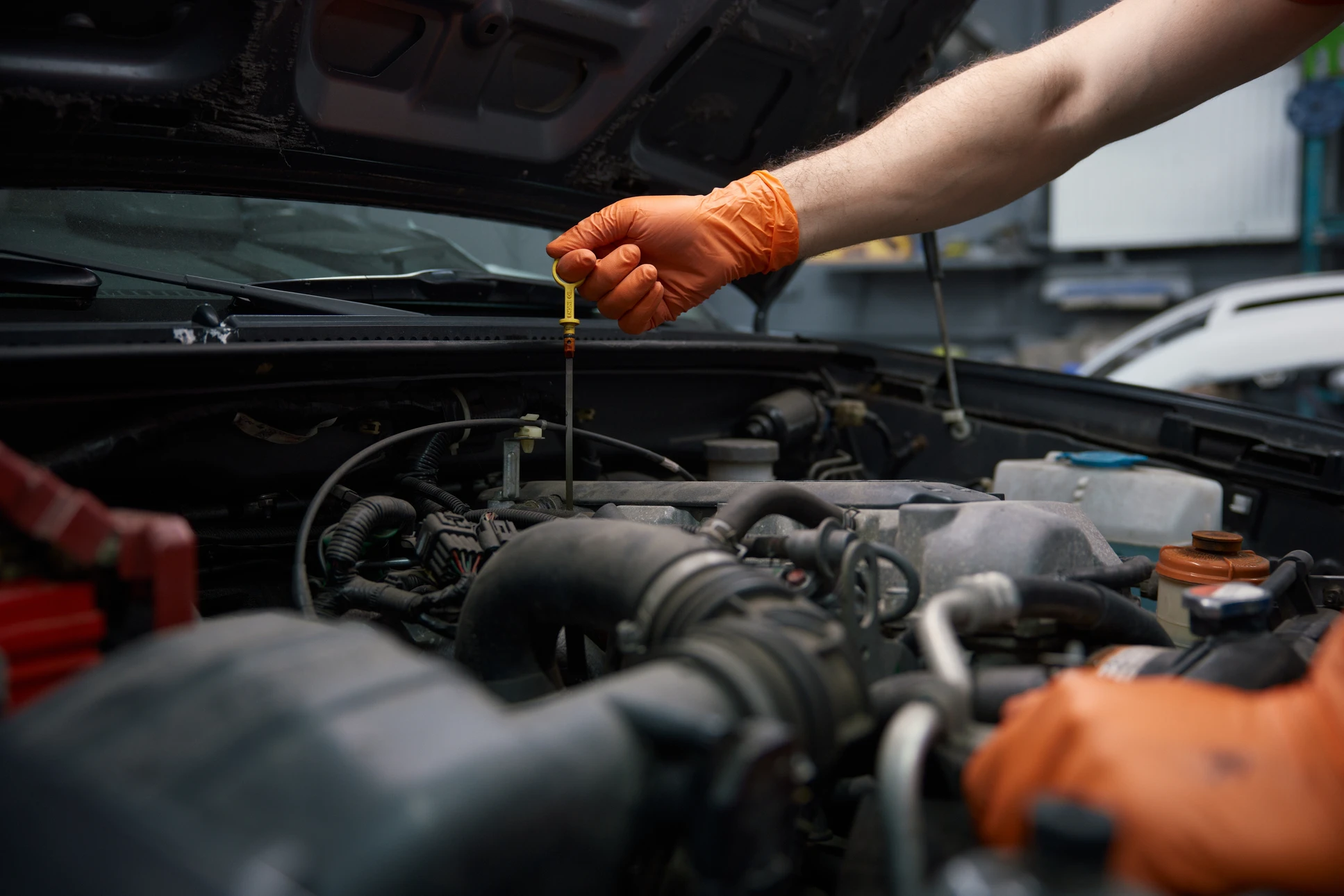 Mécanicien en gants nitrile effectuant une vidange d'huile moteur dans un garage automobile