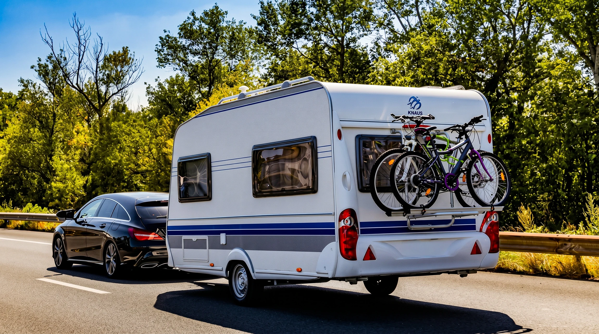 Scène extérieure avec caravane blanche et bleue tractée par SUV noir sur route goudronnée
